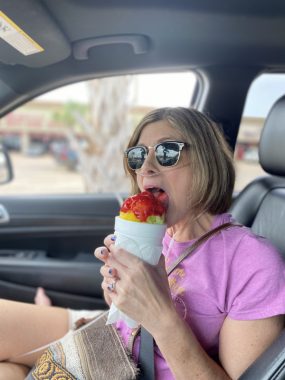 Summertime planning and avoiding heat | Pulmonary Hypertension News | In a pink T-shirt and sunglasses, columnist Jen Cueva licks a snow cone while sitting barefoot in a car