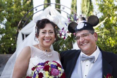PAH community | Pulmonary Hypertension News | Susie Alvarez and Perry Mamigonian smile during their Disney-themed wedding. Perry is wearing a Mickey Mouse cap and tuxedo, Susie a wedding dress and holding a bouquet of flowers