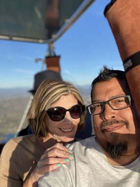 achieving goals | Pulmonary Hypertension News | Jen and her husband, Manny, smile aboard a hot air balloon as they fly over San Diego and the Pacific Ocean.