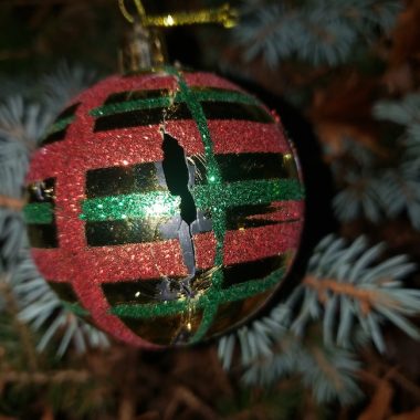 A cracked Christmas ornament hangs on a tree. 