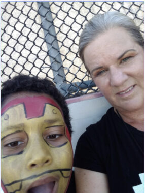 A woman and her son smile for a selfie. The woman is wearing a black T-shirt and the boy, who is leaning in toward the camera, has his face painted like Iron Man. 