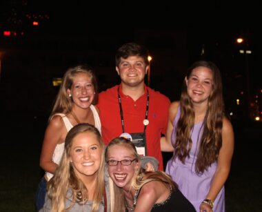 A 10-year-old photo shows five friends - four young women and one young man - posing and smiling for a group photo. The background lighting is bad so we can only see the front of the people. 