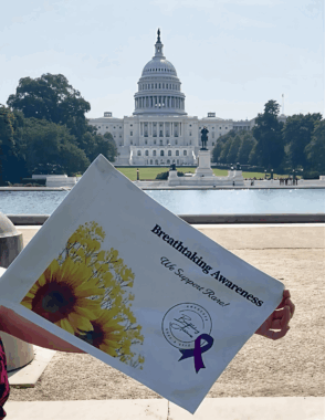 An awareness flag is shown being held by someone off the frame as the U.S. Capitol looms in the distance.