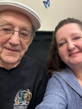 A woman takes a selfie of herself and her father, both grinning at the camera.